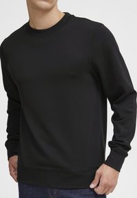 Black sweatshirt with a round neckline, long sleeves, and ribbed cuffs. Smooth texture, featuring subtle seams and a comfortable fit.