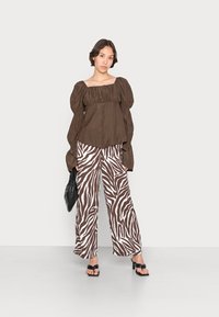 Blusa castanha de mangas bufantes com decote elástico, combinada com calças largas com estampado de zebra em castanho e branco. Acessorizada com uma bolsa preta.