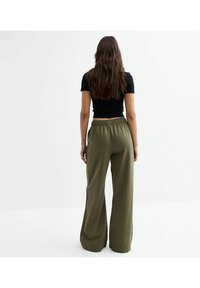 Un pantalon large, vert olive, en tissu doux. Une taille élastique avec une texture lisse et sans motifs ni accessoires visibles.