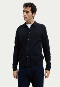 Marineblauer Wollcardigan mit kragenförmigem Ausschnitt, Knopfverschluss und zwei vorderen Taschen; verfügt über eine strukturierte Oberfläche und lange Ärmel.