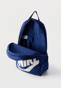 Σκούρο μπλε σακίδιο με μεγάλο λευκό λογότυπο Nike, ανοιχτό και ξεκούμπωτο, με κενό εσωτερικό και υφασμάτινη ετικέτα στο εσωτερικό.