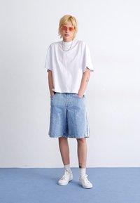 Biele oversized tričko, svetlo modré denimové šortky s bielymi bočnými prúžkami, biele tenisky a ružové slnečné okuliare. Jednoduchý, neformálny outfit.