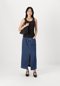 Black lace-trimmed tank top paired with a high-waisted, denim maxi skirt featuring a front slit. Accessorized with a black handbag and heels.