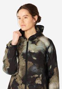 Chaqueta acolchada en una mezcla tenue de colores beige, negro y verde. Cuenta con capucha, cierre de cremallera y sutiles patrones en forma de ola en la tela.