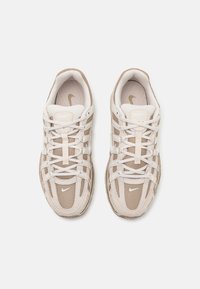 Beige sportskor med ovandel i mesh, beige överdrag, vita snören, vadderad krage och en liten vit Nike-logga på sidan.