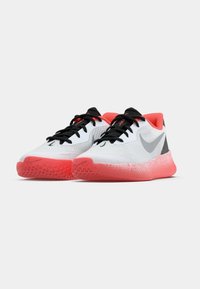 Bela atletska obutev z teksturirano zgornjo površino, črnimi vezalkami in roza gumijastim podplatom. Na strani je siv logotip, na peti pa rdeči poudarki.