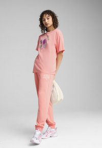 Light pink t-shirt with graphic design featuring leaves and fruit, paired with matching joggers featuring a logo print, and white sneakers.