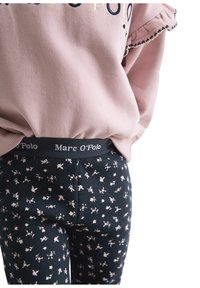 Różowa bluza z falbaniastymi rękawami na czarnych legginsach z kwiecistym wzorem. Legginsy mają markowy pas.