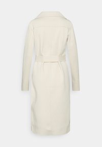 Krémový kabát z vlněné směsi s páskem v pase, dlouhými rukávy a klopovým límcem. Má tailored siluetu a zadní rozparek pro snadný pohyb.