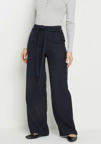 Szerokie spodnie w kolorze granatowym z paskiem w talii, plisowanym przodem i lekkiego materiału. Połączone z szarym topem z długim rękawem i czarnymi balerinkami.