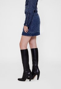 Juodos odos iki kelių aulinukai su stiletto kulniuku, pasižymintys lygiu paviršiumi ir šoniniu užtrauktuku papildomam patogumui.