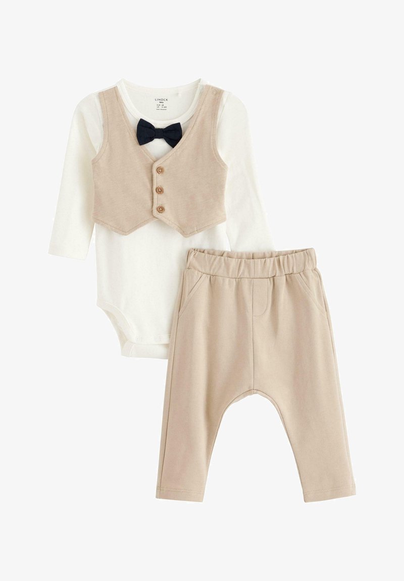 Gilet beige avec trois boutons et un nœud papillon noir sur un body à manches longues blanc, associé à un pantalon beige, doux et à taille élastique.