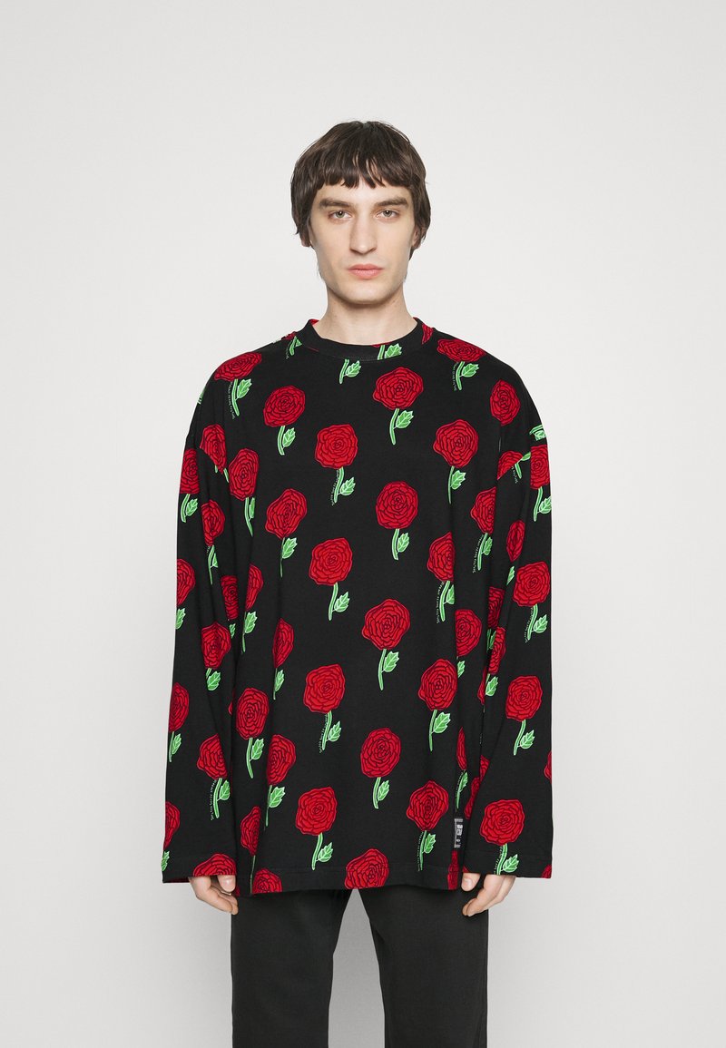 Μαύρη μπλούζα μακρυμάνικη με επαναλαμβανόμενο σχέδιο με κόκκινες τριανταφυλλιές και πράσινα φύλλα. Μαλακό ύφασμα και άνετη εφαρμογή, με στρογγυλή λαιμόκοψη.