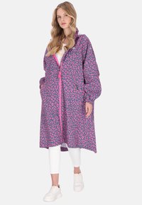 Lång, puffig jacka i lila med rosa leopardmönster, dragkedja fram, sidfickor och elastiska ärmslut. Buren över vit topp och leggings.