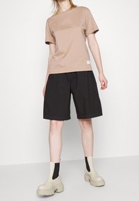 T-shirt en coton beige, coupe décontractée, associé à un short noir, longueur genou. Chaussures : bottes chunk en beige avec des chaussettes noires. Design simple, sans motifs.