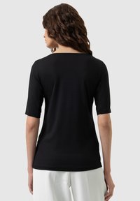 Black T-shirt with short sleeves, smooth texture, simple design, and a rounded neckline, paired with white trousers.