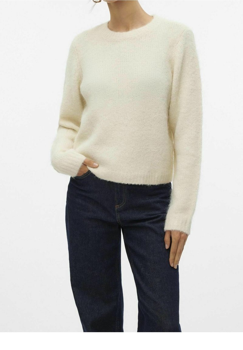Cremefarbenes, weiches Strickpullover mit rundem Ausschnitt und langen Ärmeln, kombiniert mit dunklen Jeans. Der Pullover hat eine leicht lockere Passform.