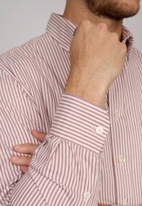 Chemise à rayures rouges et blanches avec un col, comportant un poignet maintenu par un bouton, tissu au toucher lisse.