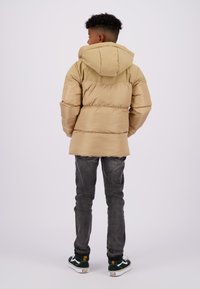 Beige pufferjack met capuchon, voorzien van een doorgestikte ontwerp en een contrasterend bovenpaneel. Draag met donkere jeans en groene sneakers.