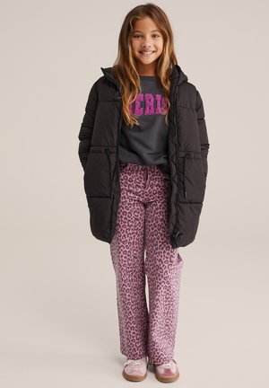 Cappotto imbottito nero con cappuccio, felpa grigia con scritte rosa e pantaloni larghi a stampa leopardata rosa. Scarpe da ginnastica chiare ai piedi.