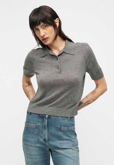 Polo gris à manches courtes avec col, fermeture par boutons, ourlet côtelé et tissu en maille texturée, associé à un jean denim bleu clair.