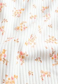 Stoff mit Blumenmuster, der kleine rosa und gelbe Blumen auf einem weißen gerippten Hintergrund zeigt und eine weiche Textur sowie ein filigranes Design präsentiert.