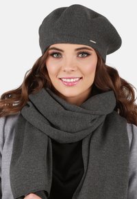 Set di berretto e sciarpa a maglia grigia, caratterizzato da una texture morbida, design accogliente e bordi a coste, indossato su uno sfondo neutro.