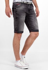 Donkergrijze denimshorts met verwering en opgerolde manchetten. Heeft rode stiksels en vijf zakken. Gecombineerd met witte sneakers.