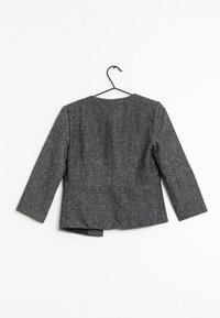 Harmaa räätälöity bleiseri, jossa on tekstitu finish, pitkät hihat, pyöreä kaula-aukko ja tyköistuva malli, roikkumassa mustalla koukulla.