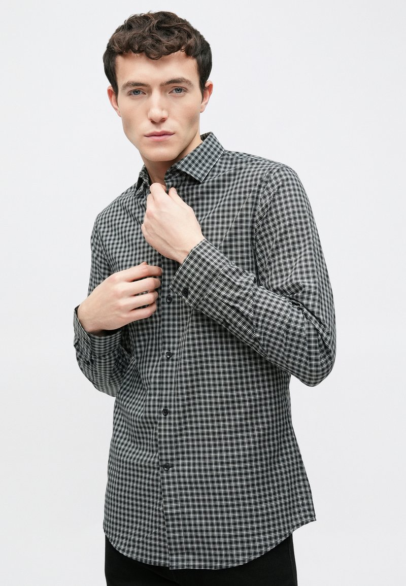 Πουκάμισο με κουμπιά σε ασπρόμαυρο καρό σχέδιο, με κανονικό γιακά, μακριά μανίκια και εφαρμοστή γραμμή. Λείος υφασμάτινος.