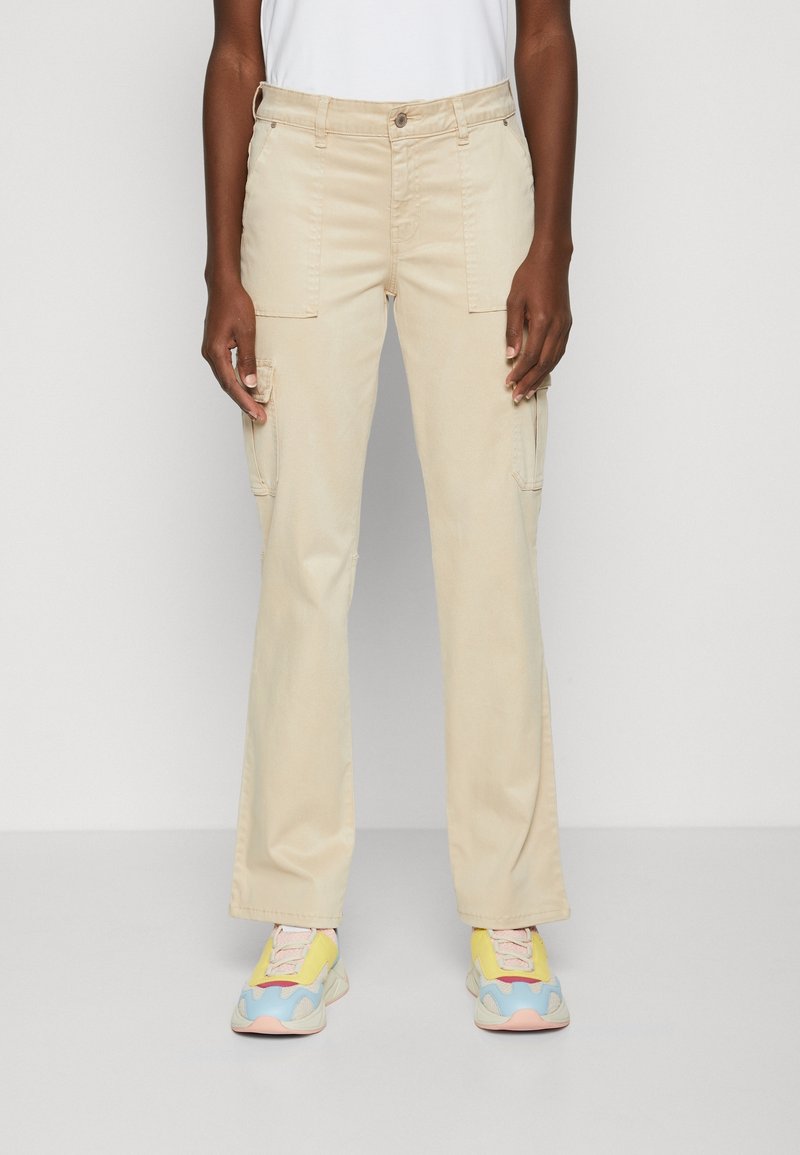 Pantalons cargo beige avec une jambe droite, deux poches avant et une ceinture robuste, associés à des baskets colorées avec des accents rose, jaune et bleu.