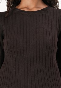 Maglione a coste di un marrone scuro con scollo a girocollo e tessuto strutturato, che enfatizza le linee verticali e una silhouette aderente.