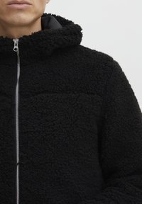 Zwarte fleece jack met een ritssluiting aan de voorkant en gevoerde capuchon, tekstuurstof en een ontspannen pasvorm met een gladde binnenvoering.