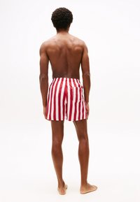 Rote und weiße gestreifte Badeshorts mit elastischem Bund und einer Gesäßtasche. Der Stoff wirkt glatt und hat eine leichte Textur.