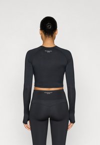 Ensemble de vêtements de sport noirs comprenant un haut à manches longues court et un legging taille haute, fabriqués en tissu extensible, avec un logo en détail à l'arrière.