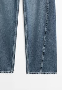 Rechte blauwe spijkerbroek van denim met zichtbare naden en een lichte vervaging, plat afgebeeld op een witte achtergrond.