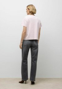 Lichtroze katoenen t-shirt met een cropped ontwerp, gecombineerd met hoge, donkergrijze jeans en bruine hoge hakken.