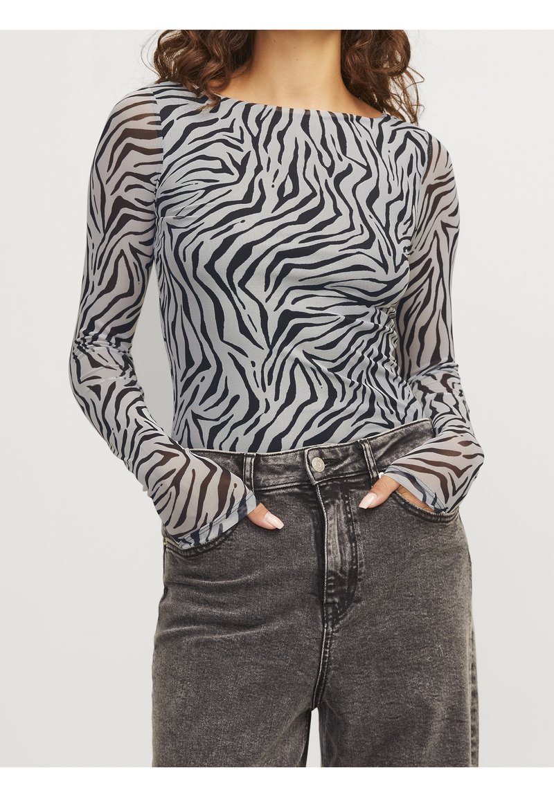 Top met lange mouwen met een zebraprint in zwart en grijs, voorzien van doorschijnende mesh stof en een ronde halslijn, gecombineerd met donkere spijkerbroek.