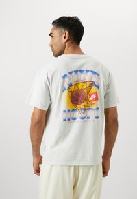 Lys grå bomulds t-shirt med et farverigt grafisk design på ryggen, der viser en basketball og teksten "NIKE HOOPS SUMMER LEAGUE." Korte ærmer.
