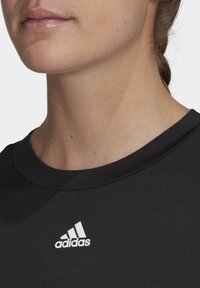 Svart sporttröja med rund hals och korta ärmar. Har en vit Adidas-logga på vänster bröstområde. Slätt tyg med mjuk struktur.