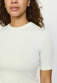 Gai beigtas īsās piedurknes T-krekls ar apaļu kaklu, izgatavots no mīkstas, teksturētas auduma. Tam ir smalka rakstaina un cieši pieguļoša forma.