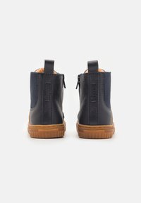 Botas de cuero náuticas hasta el tobillo con paneles elásticos laterales, lengüetas traseras y suelas de goma texturizadas. Presentan un acabado suave y acentos en colores neutros.