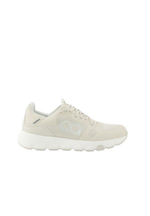 Beiger Sportschuh mit weißer dicker Sohle, Mesh-Seitenteilen, Logo und Schnürsenkeln, von der Außenseite vor weißem Hintergrund gezeigt.