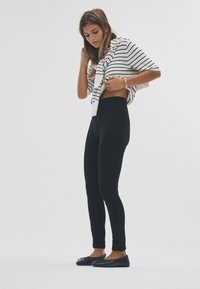 Fekete, magas derekú leggings, fehér-fekete csíkos felsővel, amely vállra van dobva. Simogató textúra, minimalista dizájn.