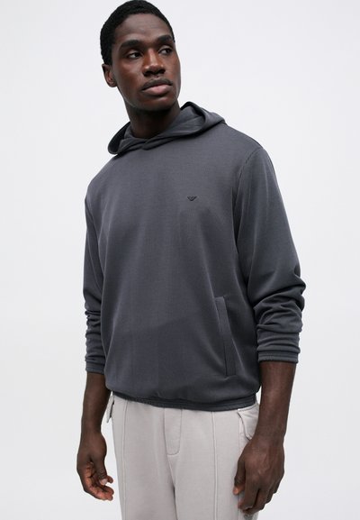 Γκρι ριγέ φούτερ με κουκούλα, μακριά μανίκια και εμπρόσθια τσέπη. Υφασμάτινη υφή με διακριτές ραβδώσεις. Συνδυασμένο με ανοιχτό γκρι παντελόνι.