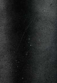 Gros plan d'une surface noire texturée avec de petites taches blanches éparpillées de manière inégale.