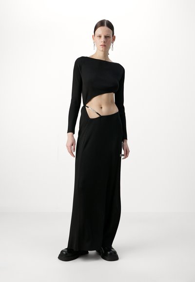 Černý žebrovaný dvoudílný outfit zahrnující zkrácený top s dlouhým rukávem a maxi sukni s vykrojením. Materiál je elastický; kalhoty mají řetízkovou dekoraci.