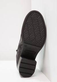 Suela de zapato negra con superficie texturizada y un patrón de zigzag, con un acento lateral y detalle de marca. Hecha de goma y materiales sintéticos.