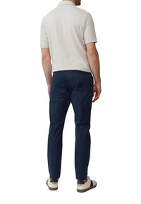 Hellgraues Kurzarm-Polohemd, marineblaue Chinos und weiße Schuhe mit schwarzen Akzenten. Der Stoff wirkt glatt und hat eine normale Passform.