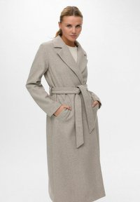 Cappotto lungo beige in lana con cintura, ampi rever e tasche laterali. Tessuto morbido e vestibilità su misura.